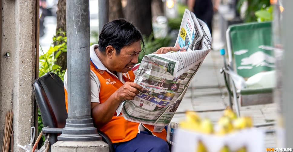 Таксист - мотобайщик читает газету в Бангкоке